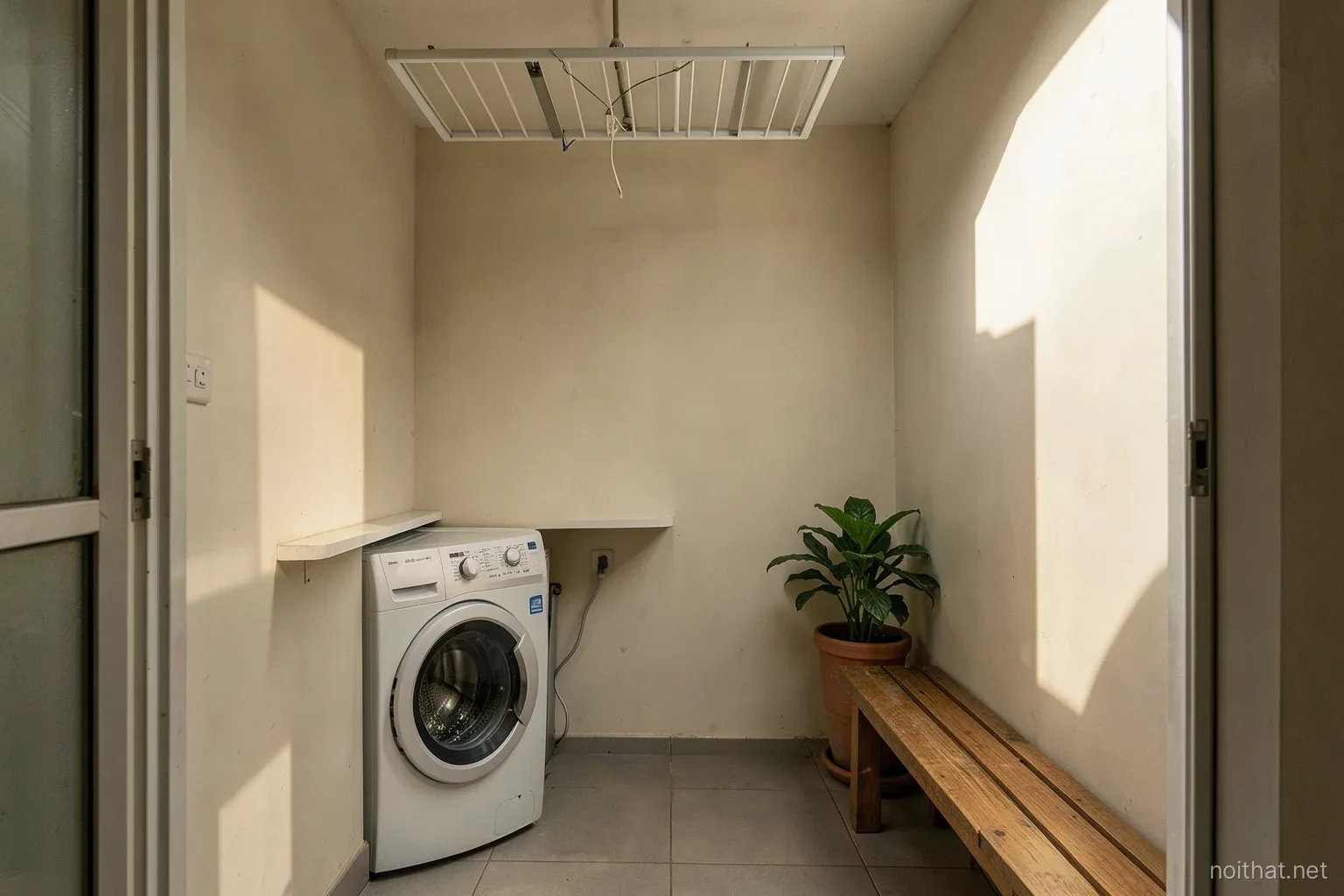 Compact Vietnamese apartment loggia after makeover, washing machine under a slim shelf at one end, ceiling drying rack, small wooden bench and potted plant at the other end, late afternoon sun