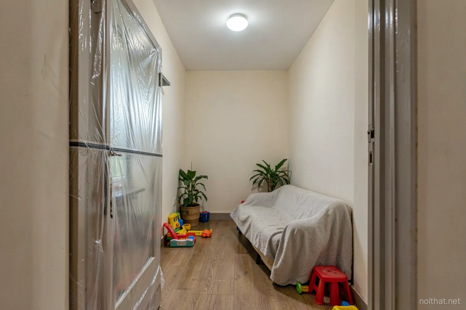 Doorway of a Vietnamese bedroom sealed with clear plastic sheeting and a zipper, dust sheet over a sofa outside, child toys pushed to one side, cool hallway light